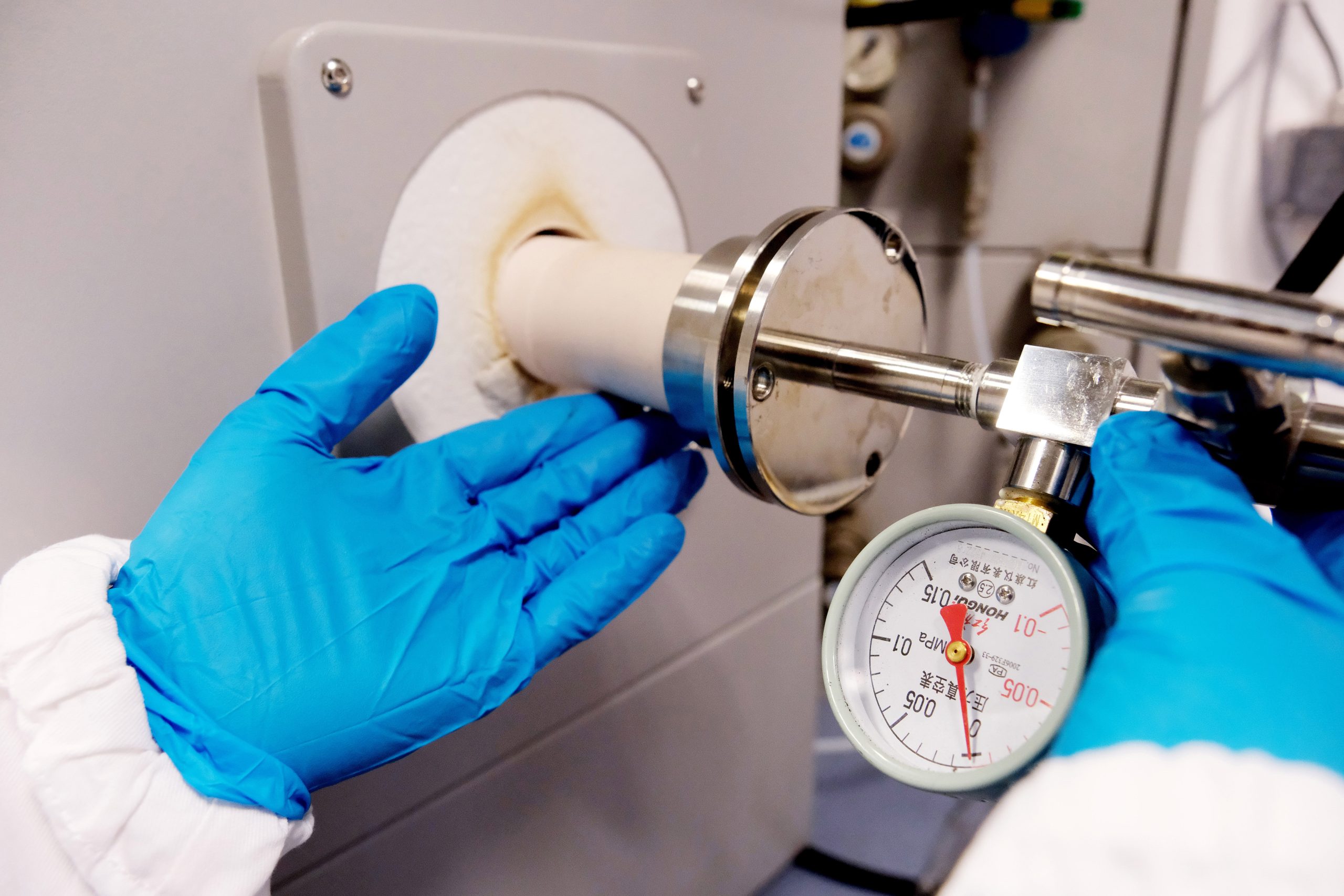 Scientist checking pressure in a laboratory setup, representing the synthesis and characterization of nanoparticles and nanocomposites using controlled experimental conditions and flow-reactor systems.