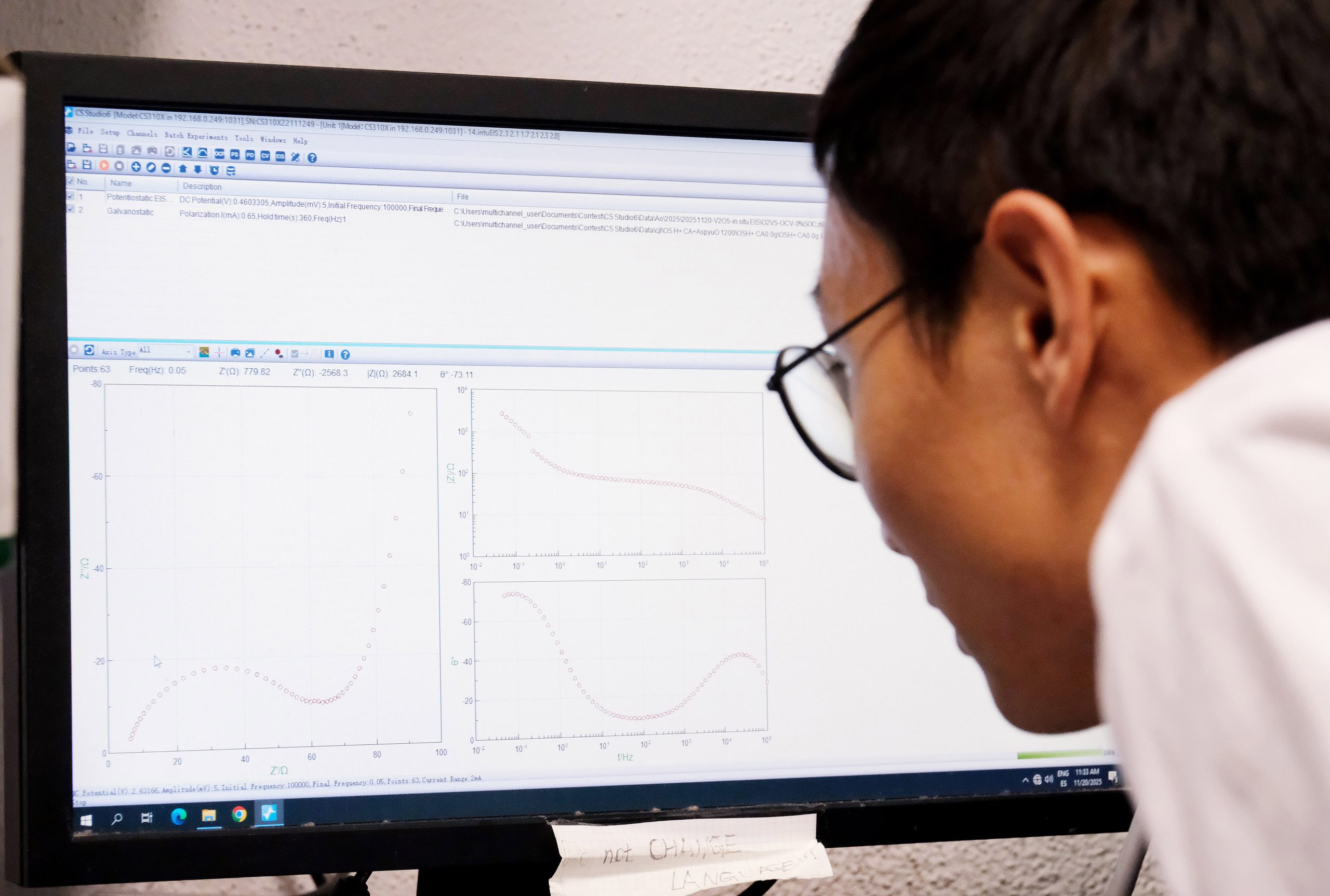 Scientist analyzing computer screen with graphs and data visualizations, representing research on advanced battery materials, electrochemical systems and energy storage performance optimization.