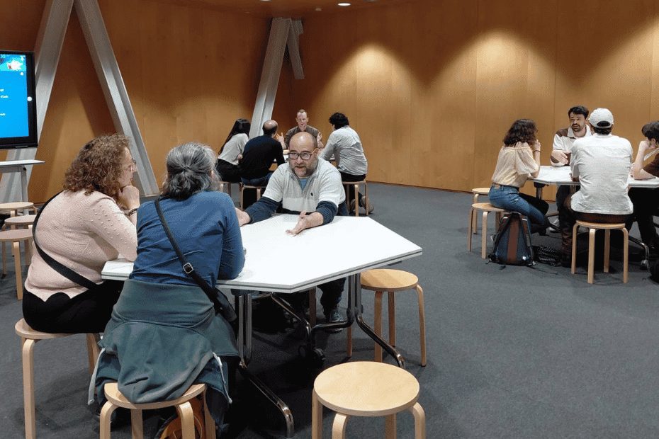 A group of people engaged in small group discussions at white tables during the Festival 10alamenos9 event.