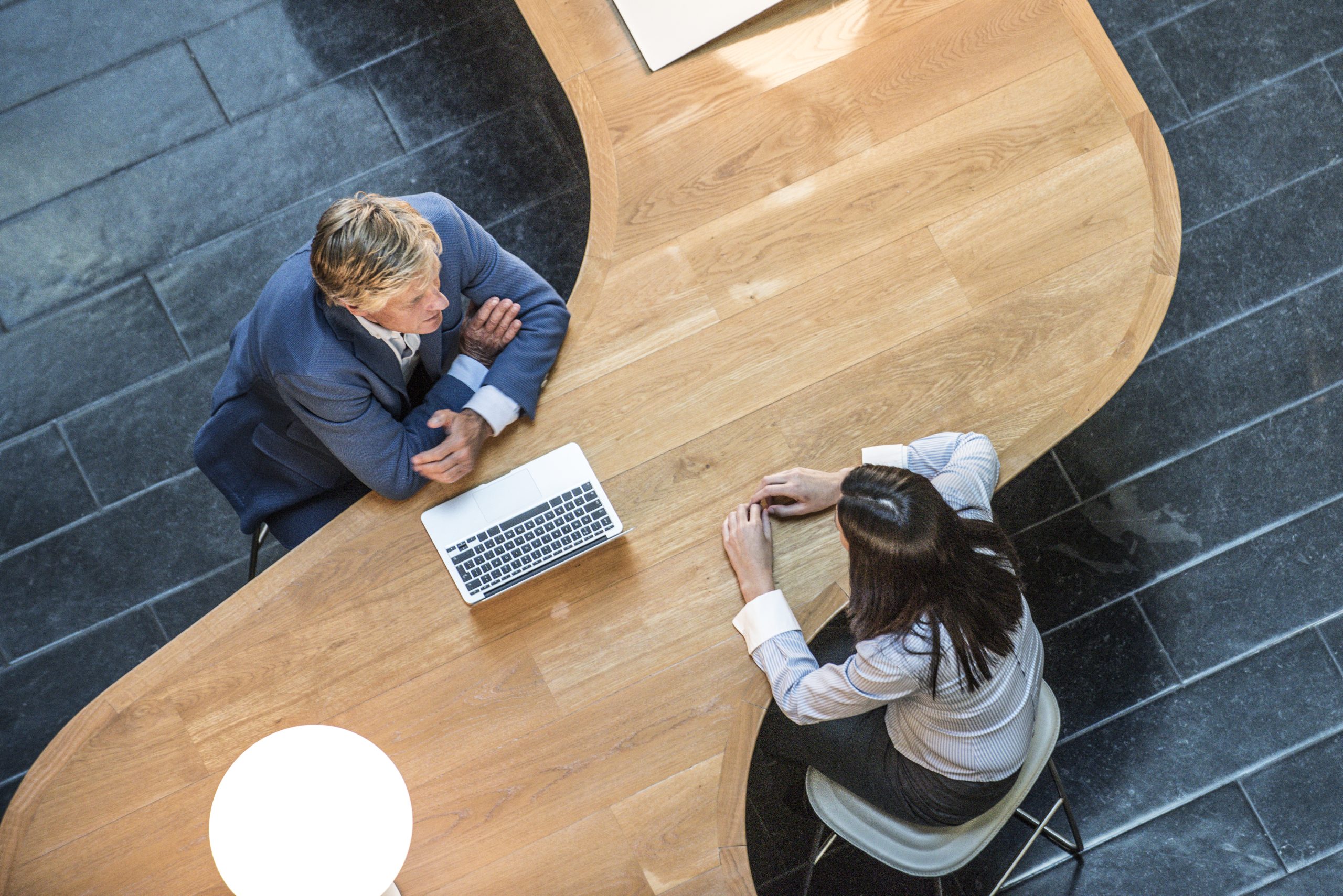 Overhead view of two professionals meeting at a curved wooden table, reflecting strategic planning, control, and coordination of energy research projects.
