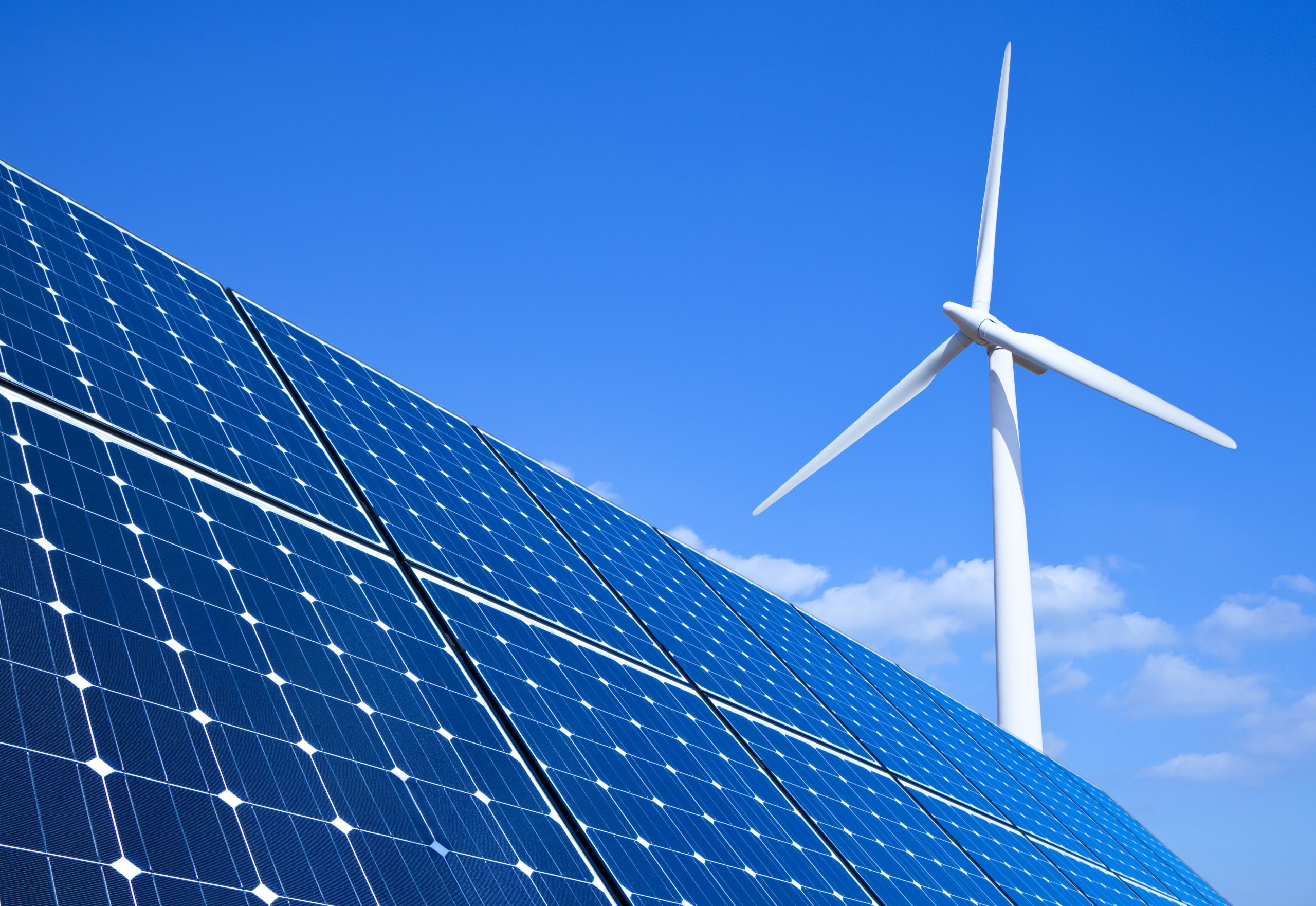 Solar panels and a large wind turbine against a bright blue sky, showcasing IREC's role as an international reference in offshore and renewable energy research through PLEMCAT.